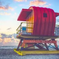Tips for visiting Miami on a budget cover photo of a colourful lifeguard stand facing the ocean at sunset