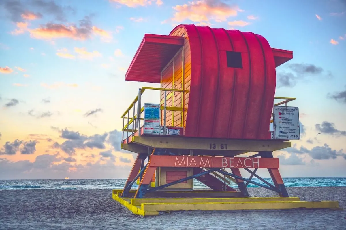 Tips for visiting Miami on a budget cover photo of a colourful lifeguard stand facing the ocean at sunset