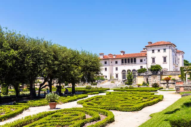 Stately Italian style 3 storey white mansion of Vizcaya museum behind the manicured gardens and white stone pathways leading to it.