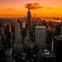 Perfect Itinerary for One Day in New York City (By A Local) header image of the New York skyline from above at sunset backed by shaed of orange and purple