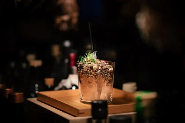 Short cockatil in a tumbler on a dark bar surrounded by cocktail condiments which are out of focus