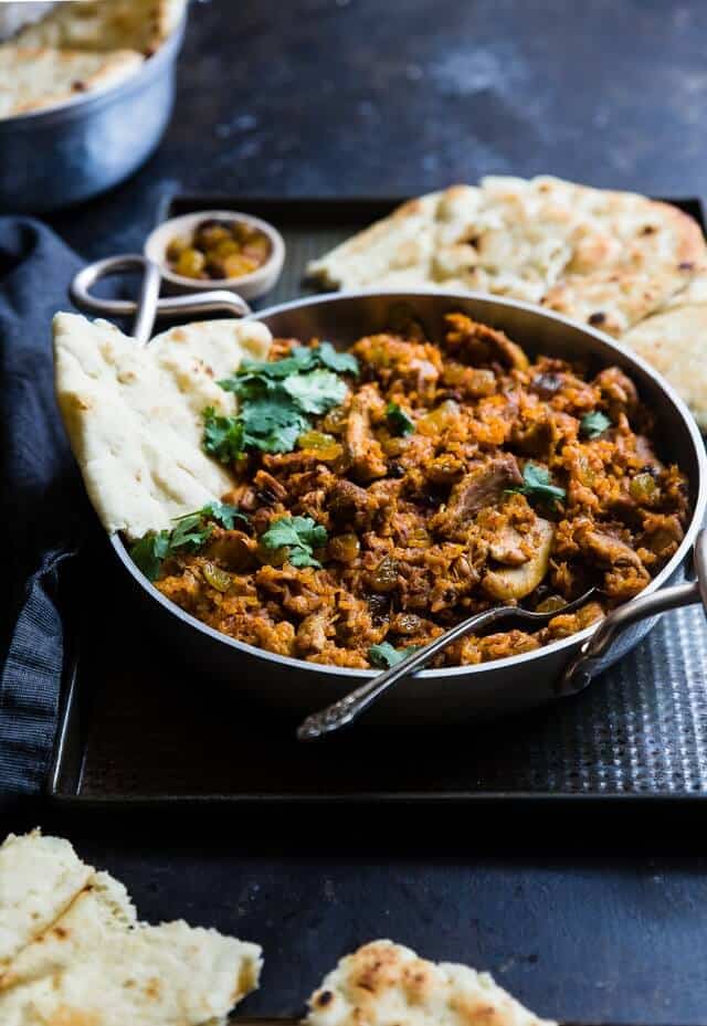 Indian curry in a metal bowl with a popodom sticking out of the curry and another on the side of the dish