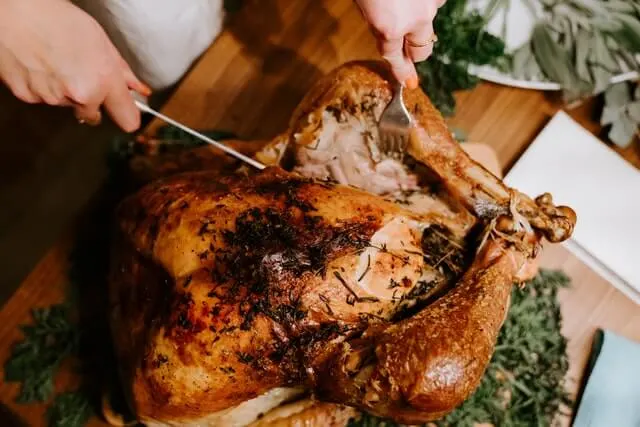 Roast Chicken on a wooden table with hands honding carving implements carving the brid