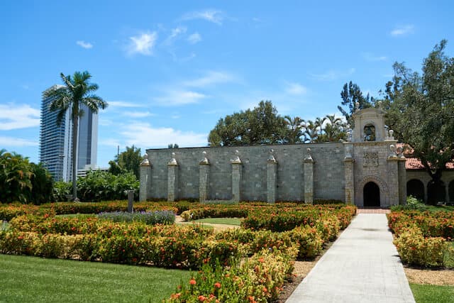 Spanish stone monastary surrounded by manicured gardens under a clear blue sky