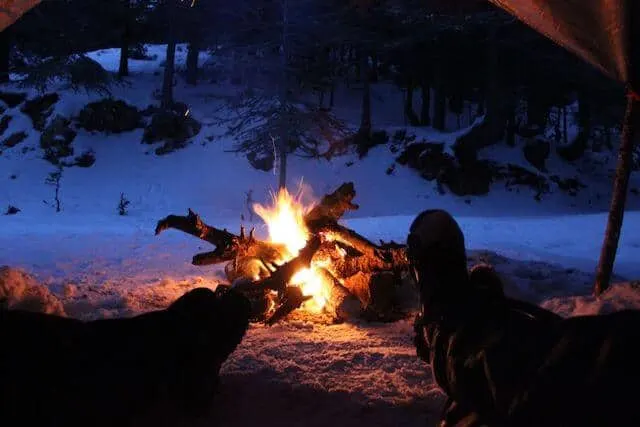 Colorado Camping looking out of the open door of the tent, two sets of legs and feet stickout out towards the campfire outside with a snowy bank in the background