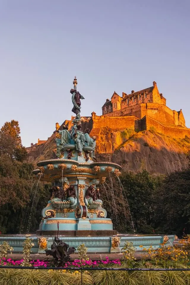 Princes Street Gardens Edinburgh behind the fountain looking up towards the castle on the hill behind it bathed in light at sunset
