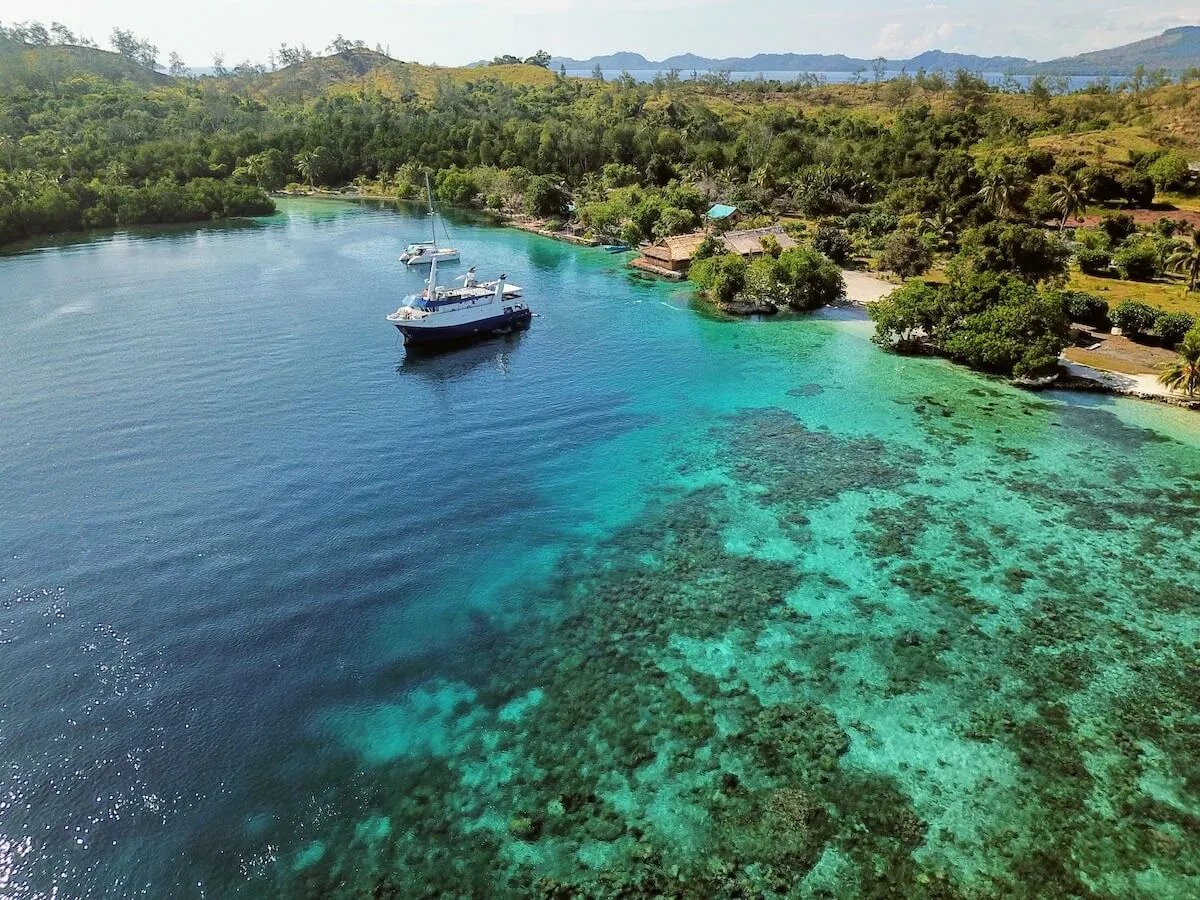 Solomon Islands Facts to know before you go - aerial shot of the Russell Islands with a small ship anchored off the shore with lighter patches of coral reef