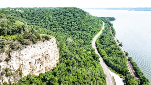 Great River Road Wisconsin winding along the side of the river flanked by green trees either side