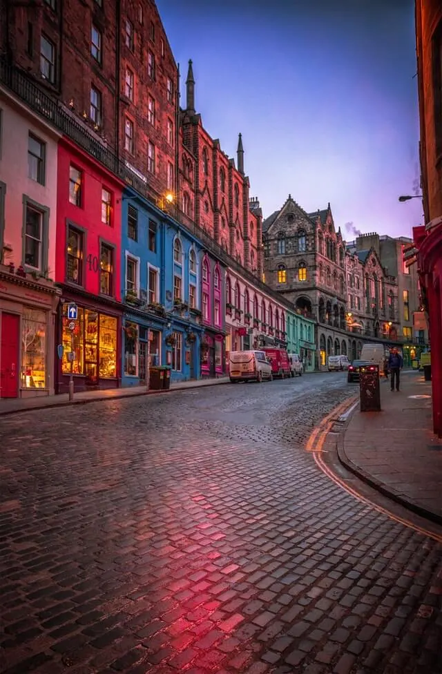 Curved and Cobbled Victoria Street, lined with colourful buildings light up at dusk 