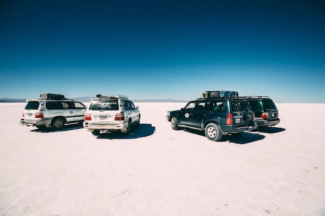 Four 4x4 off road venhicles with roof racks parked in a semi circle facing into a white sand desert