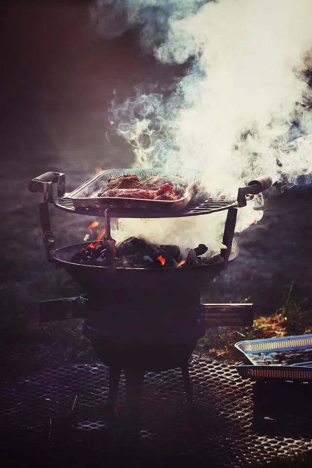 Meat cooking in a foil dish on top of a smoking coal BBQ