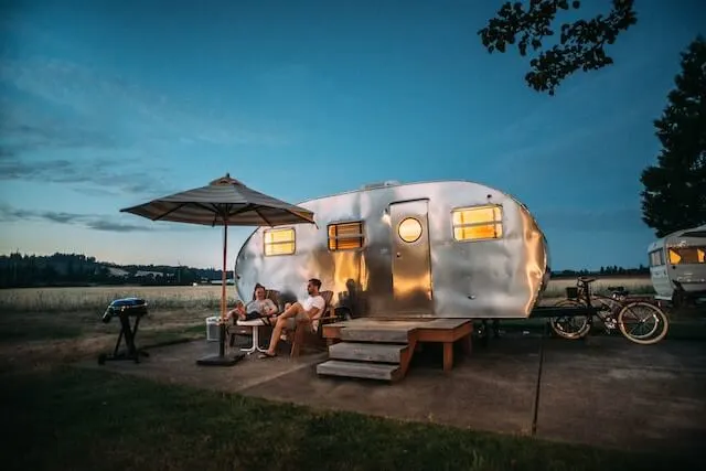 Old caravan with deck outside, two people in deck chairs with a drink in hand sat outside at dusk