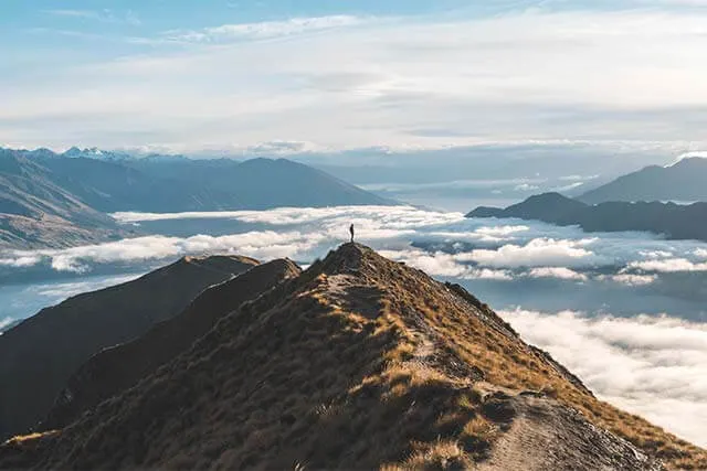 Man wearing a backpack standing at the end of Roy's Peak Track, with clouds all around