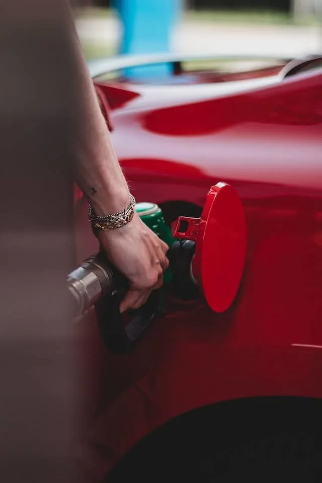 A Womans hand holding a green petrol pump putting gas into a red car
