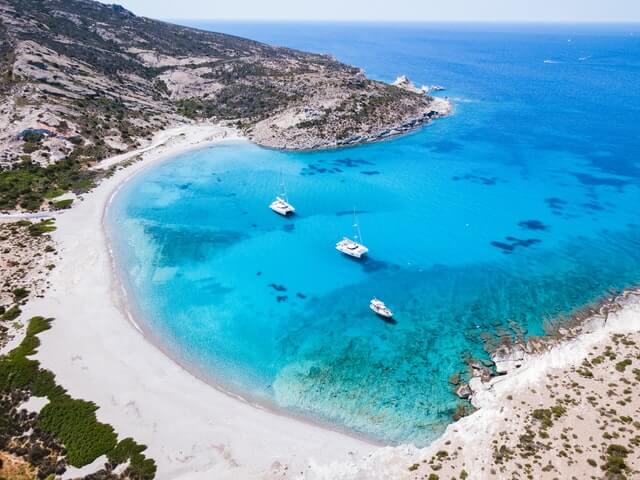 Half moon shaped bay, clear blue water against white sands, 3 boats anchored in the water just off the shoreline