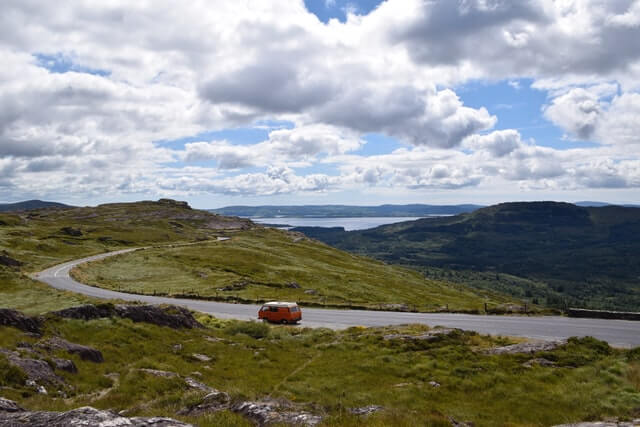Best Road Trips in Europe- Wild Atlantic Way image of a car on the road, surrounded by green fields with the ocean in the distance