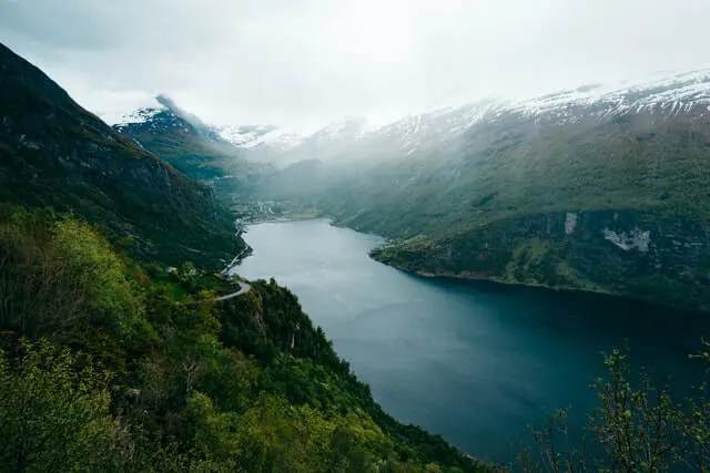 Fjord Route Norway image of a misty body of water surrounded by green hills and snowcapped mountains