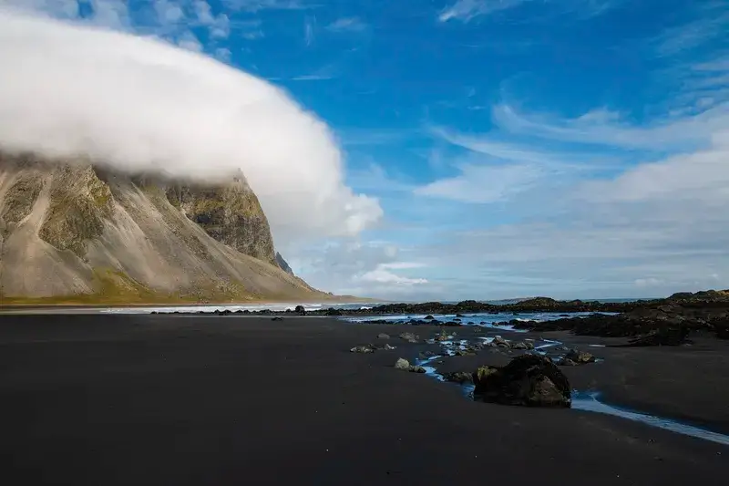 Black sand beach under a blue sky with white fluffy clouds