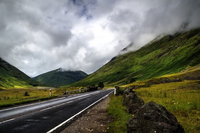Norway Road Trip - a black bitchumen road under a cloudy sky at the base of green hills