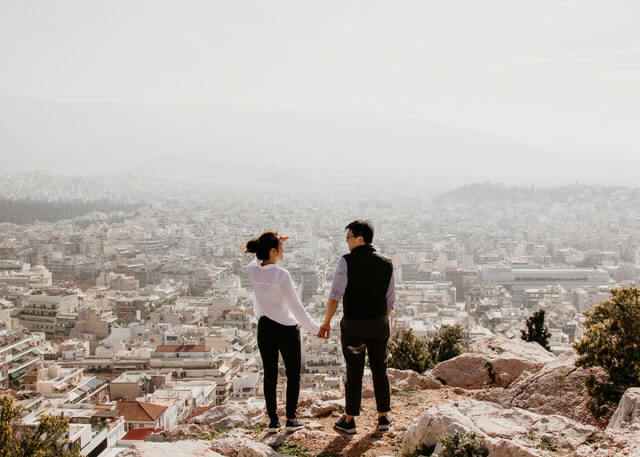Couple holding hands standing on a ledge overlooking a city
