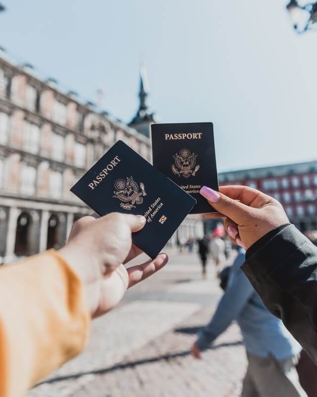 Man and womans hands holding their blue US passports in front of them in a city square