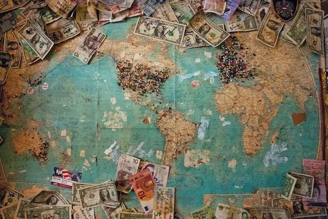 Vintage looking map covered in push pins and surrounded by notes of different currencies