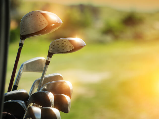 Golf clubs in focus in front of the fairway with the sun reflecting off the clubs