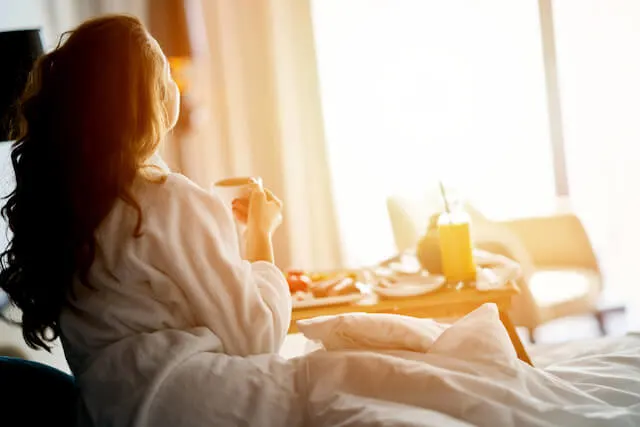 Where to Stay in Auburn California - woman wearing a white robe sitting on a bed, breakfast on a tray in front of her