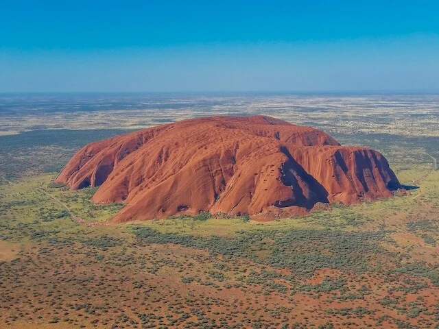 Large Red Monolithe, Uluru standing tall surrounded by the flat red earth of the Outback under a blue sky