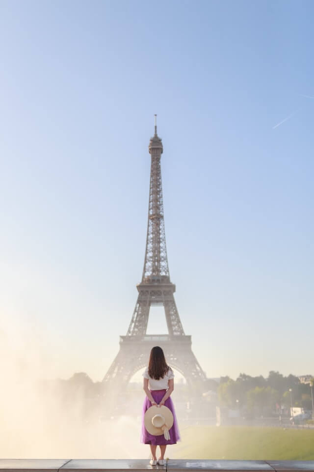 Woman in white shirt and purple skirt facing away from the camera looking towards the Eiffel Tower in the distance