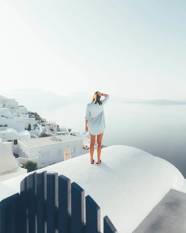 Woman wearing a blue shirt dress standing onto of a while domed roof looking out towards the ocean