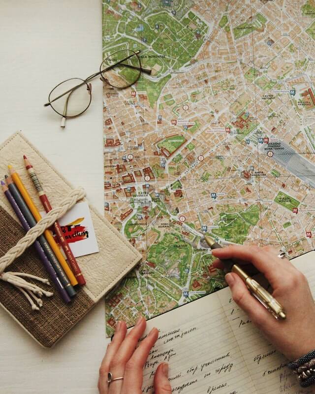Womans hands writing in a notebook with a city map in front of her on the table