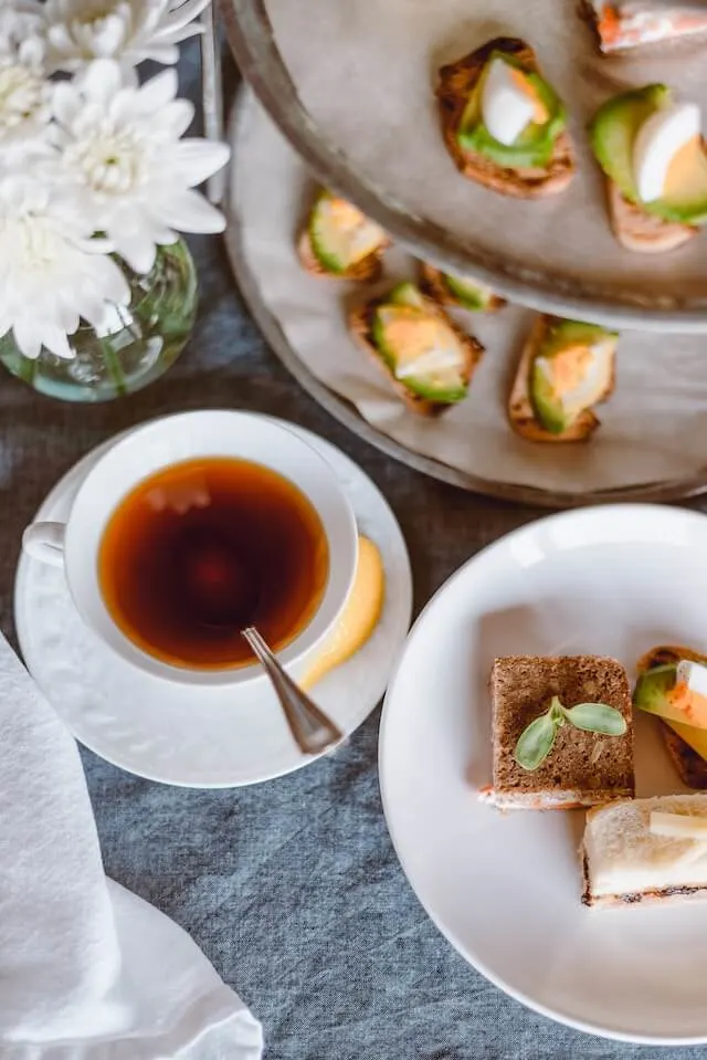 Top down shot of an afternoon tea setup with tea in a cup and saucer, and circular plates with tiny sandwiches and cakes