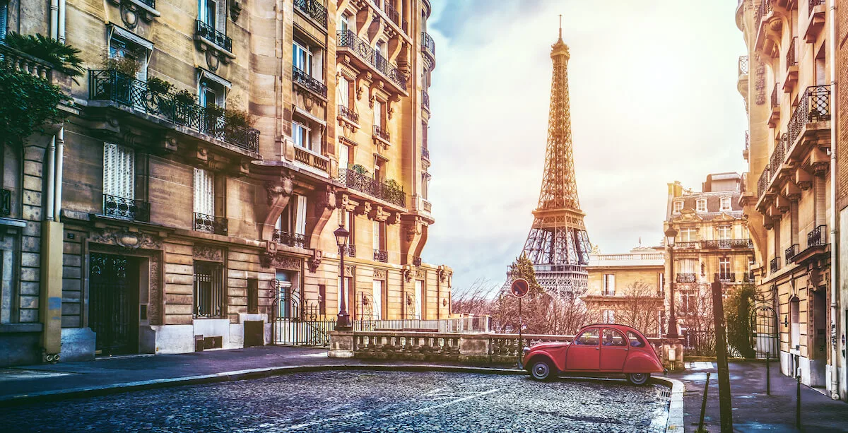 Hidden Gems in Paris cover photo of a car parked on a raised street, brick buildings either side with the Eiffel tower in the background