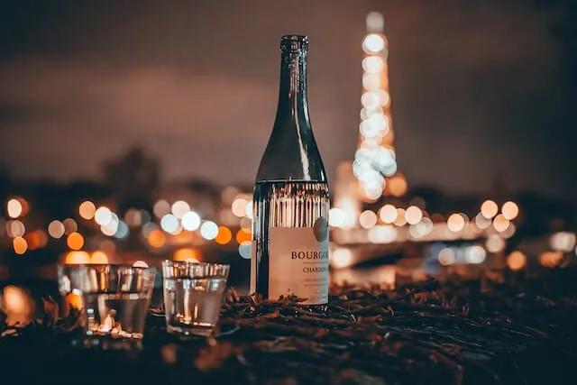 Wine bottle and two glasses in focus, with the eiffel tower lit up out of focus behind