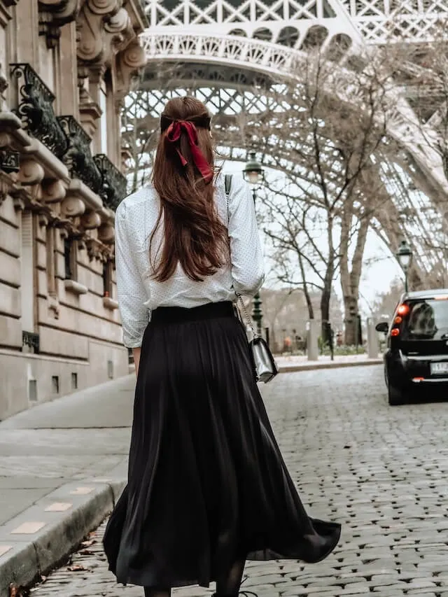 Woman in long black skirt and white long sleeved shirt with dark red ribbon in hair in from od the Eiffel Tower