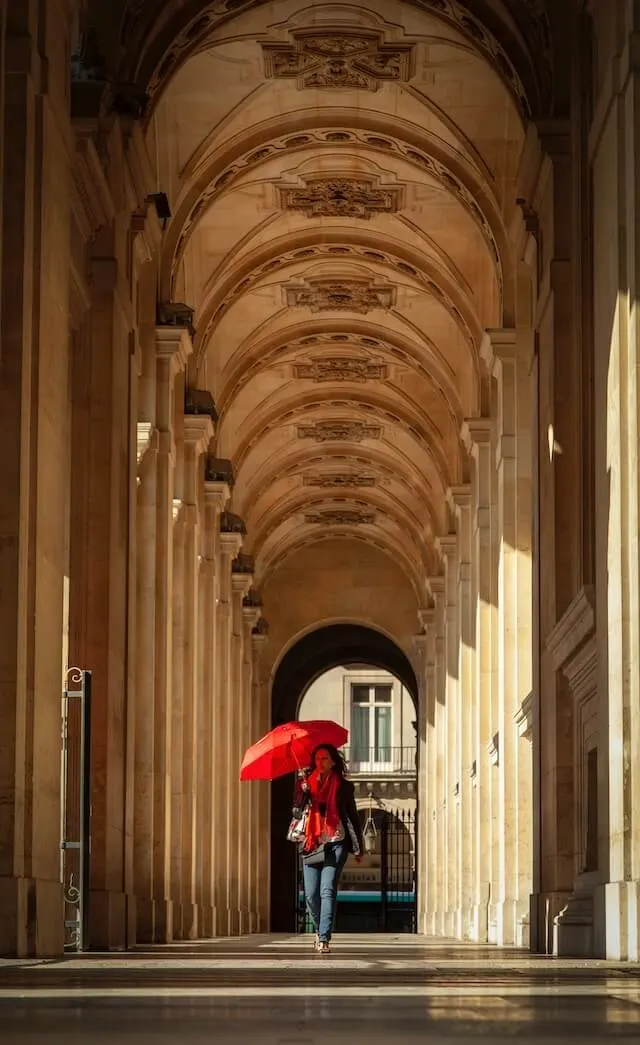 Woman with a red umbrella under a covered passageway at the Louvre