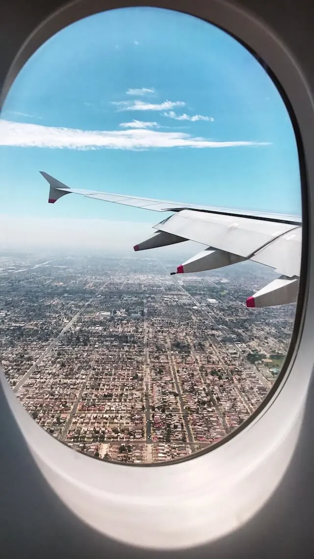 Airplane window looking out to the wing, a blue sky above and a city grid below