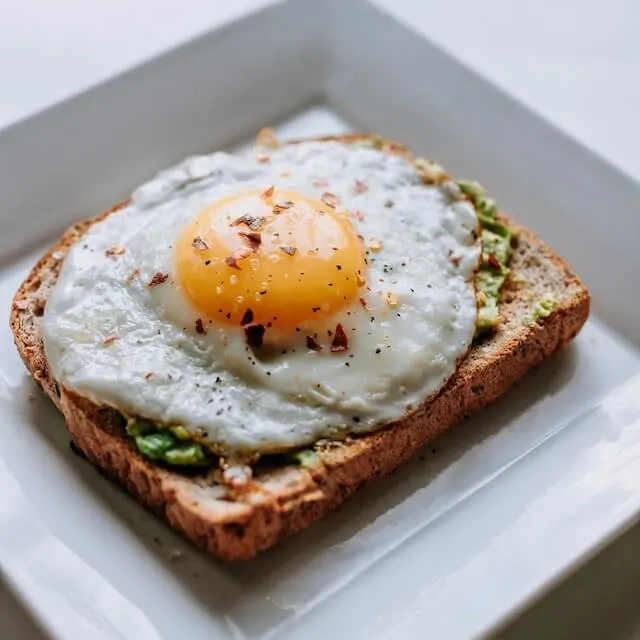 Fried egg on avocado toast on a white square plate