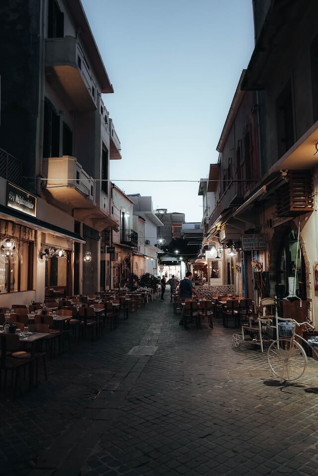 Street of Chania Town at dusk, restaurant lights on above outside table and chairs
