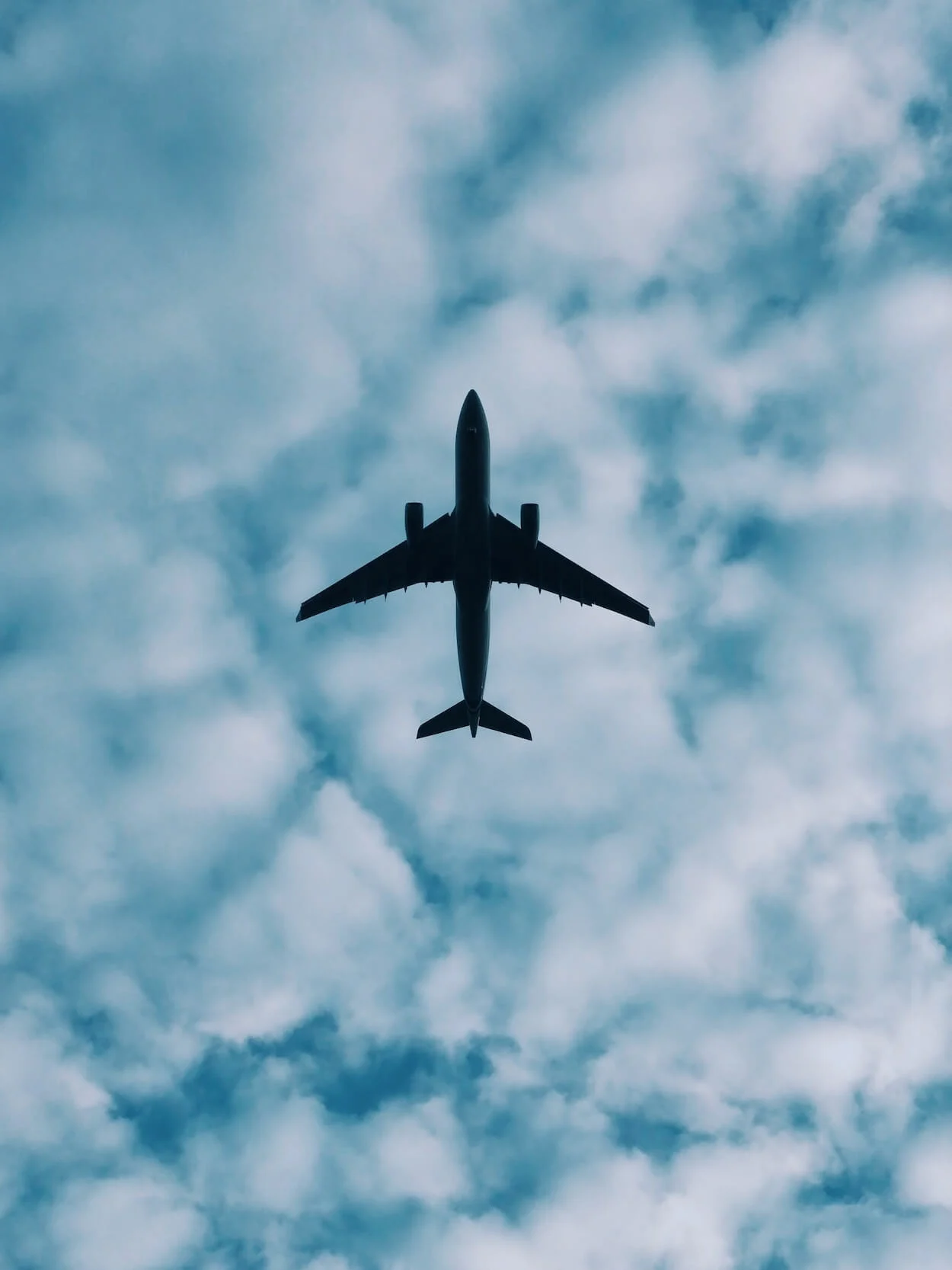 Tips to Prevent Jetlag, How to Fix Jetlag - pinterest image of the silhouette of a plane flying in a blue sky covered with white fluffy clouds