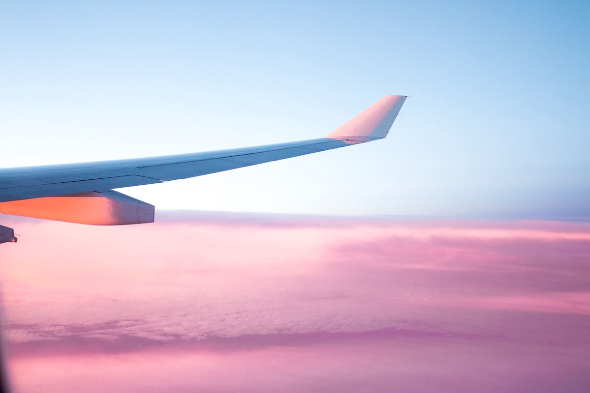 Tips to Prevent Jetlag + Remedies from Jetlag cover photo of the wing of an airplane in the sky with a pink sunset background