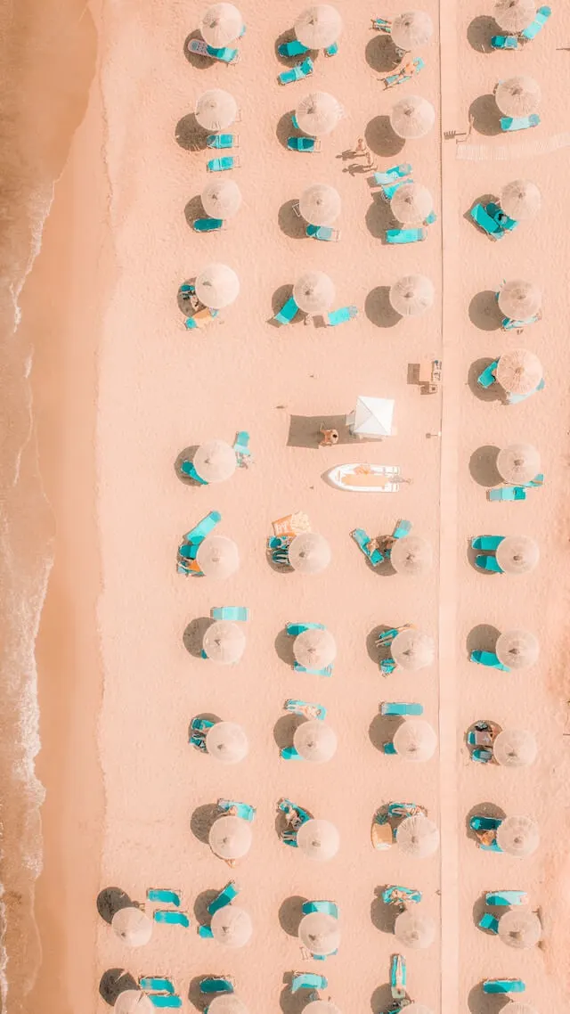 Top down drone shot of umbrellas and parasols lined up on a pinkish beach