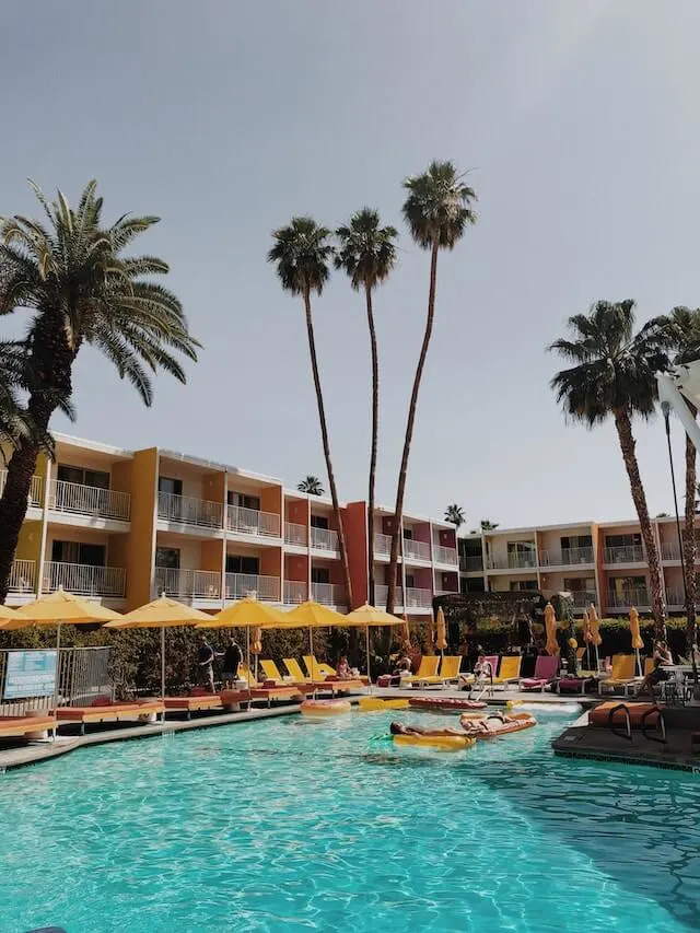 An art deco 3 storey hotel, colourful walls, a pool between the two connected L shaped buildings, palm tress sprouting up around the grounds