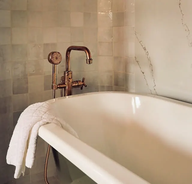 White bathtub in a tiles bathroom, a white towel hanging over the corner of the bath