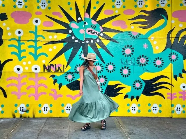 Woman in blue long dress in front of a yellow, blue and pink street art mural in Belltown