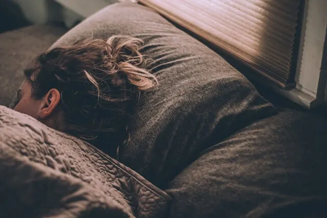 Woman sleeping in bed with grey pillowcase and comforter