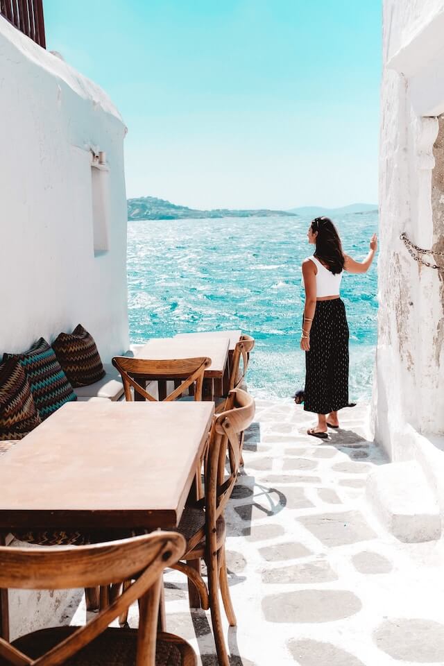 Woman standing between two whitewashed buildings next to the ocean on Mykonos