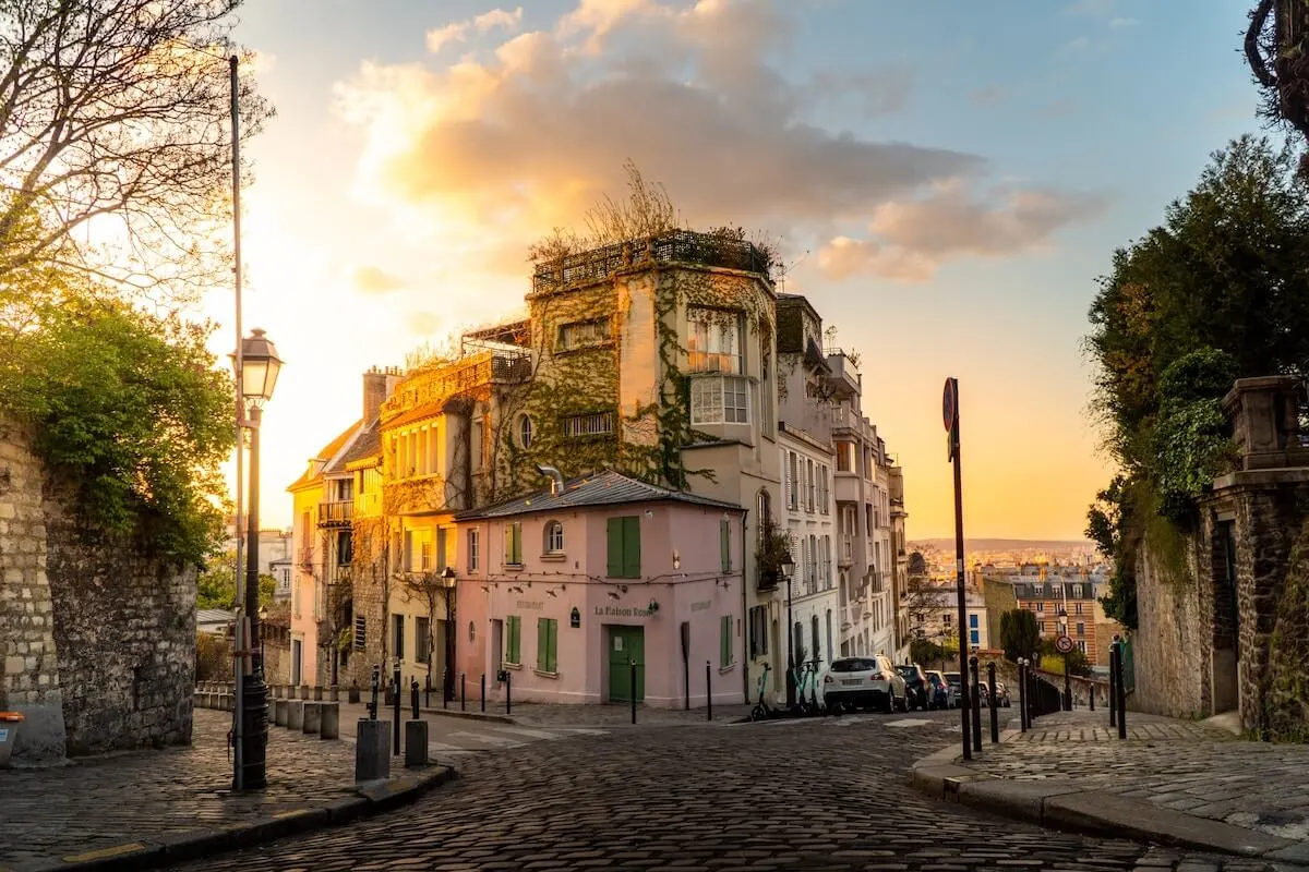 Prettiest Streets in Paris cover photo of two cobbled streets diverging around a pink house at sunset.