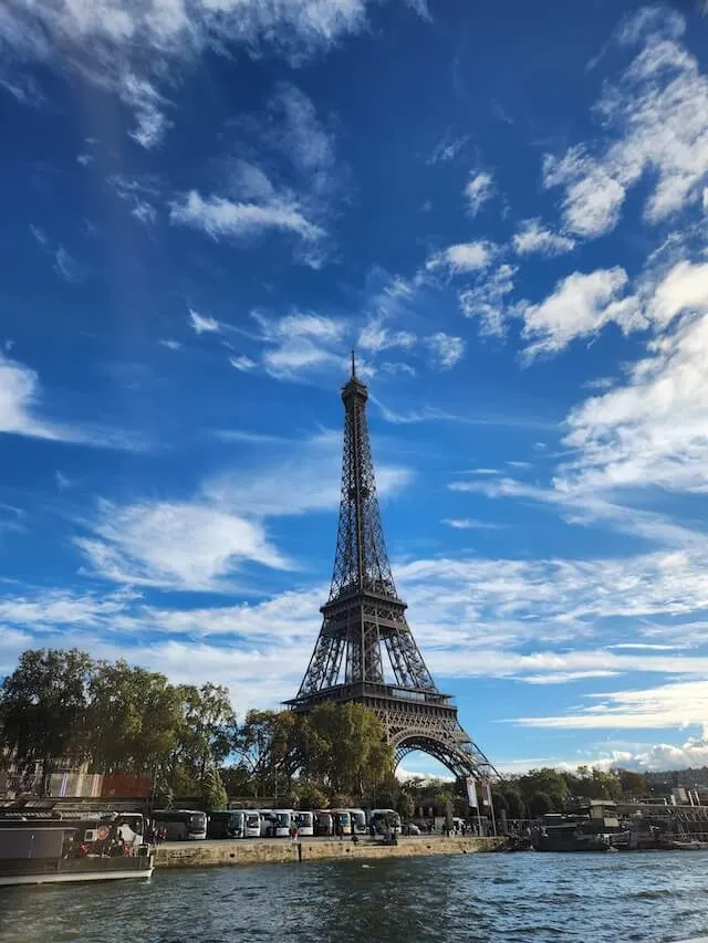 Eiffel Tower from the Seine, the river in the foreground, the sky a light shade of blue with some white wispy clouds